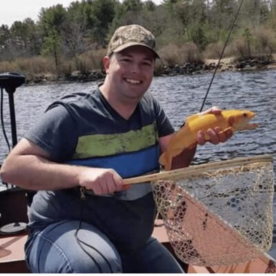 A man in a boat holding an orange fish.