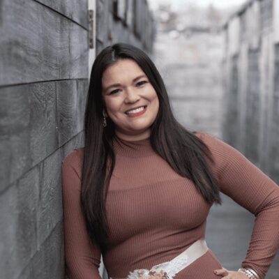 A woman in a brown dress leaning against a wall.