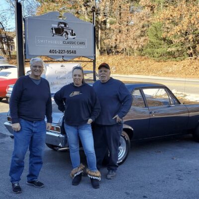 Three people standing in front of a classic car.