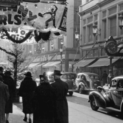 A black and white photo of people walking down a street.