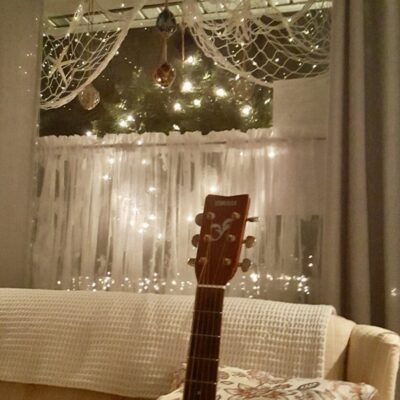 A guitar sitting on a couch in front of a window.