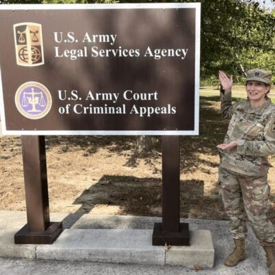 A woman in uniform standing in front of a sign that says u s army legal agency.
