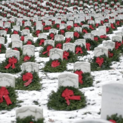 A group of headstones with red bows in the snow.