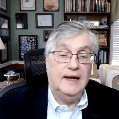 A man in glasses sitting in front of a desk.