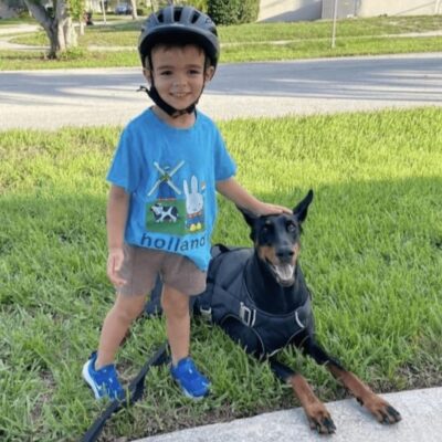 A young boy wearing a helmet next to a doberman.