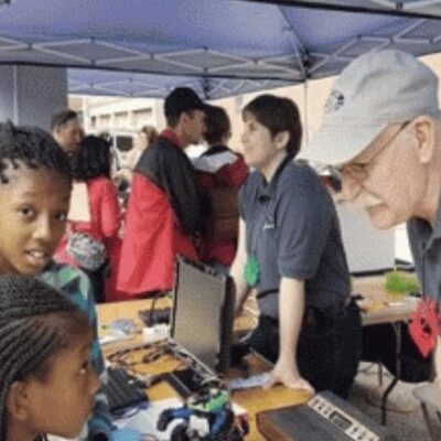 A group of children are looking at a computer at an outdoor event.