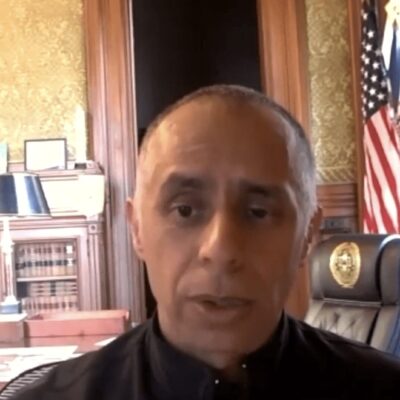 A man in a black shirt is sitting in front of an american flag.