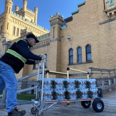 A man pushing a cart full of christmas decorations in front of a building.