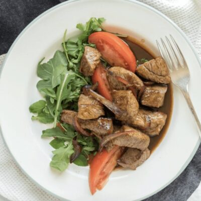 A plate with steak, tomatoes and arugula.