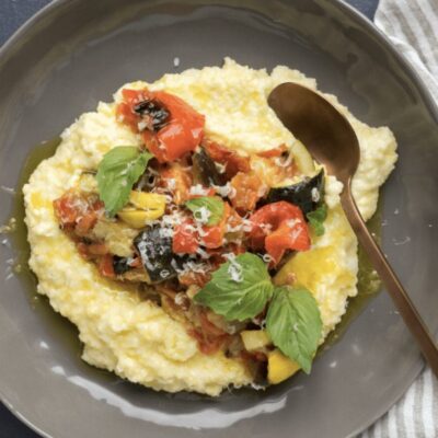 A plate of gnocchi with vegetables and basil.