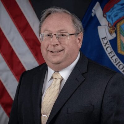 A man in a suit and tie standing in front of an american flag.