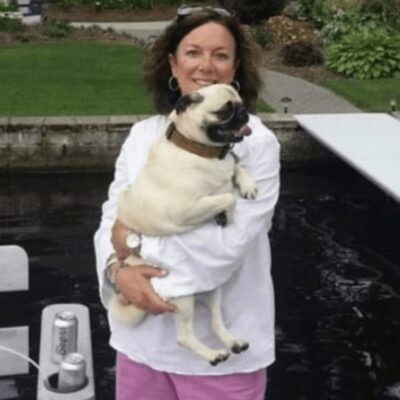 A woman holding a pug on a boat.