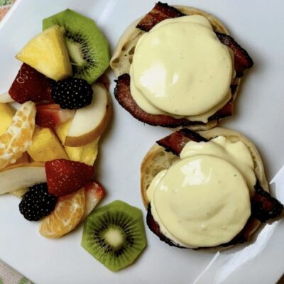Two eggs benedict with fruit on a white plate.