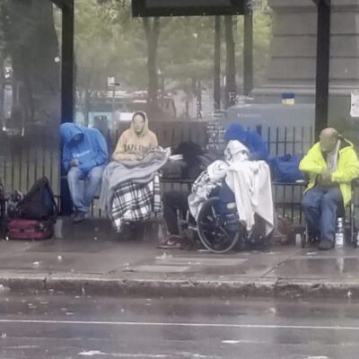 A group of people sitting on a bench in the rain.