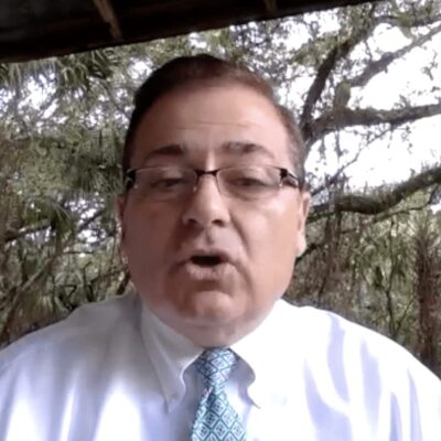A man wearing glasses and a tie in front of a tree.