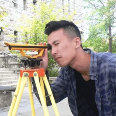A young man looking at a construction site with a surveyor's tool.