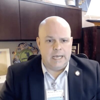A bald man in a suit sitting in front of a desk.