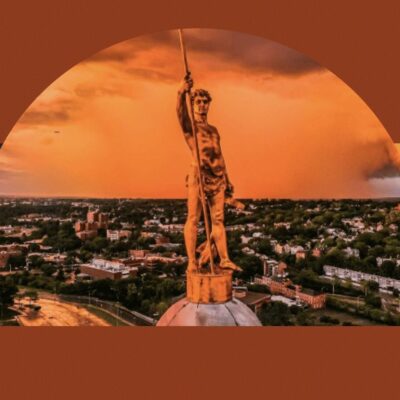 An image of a statue on top of a building with an orange sky.