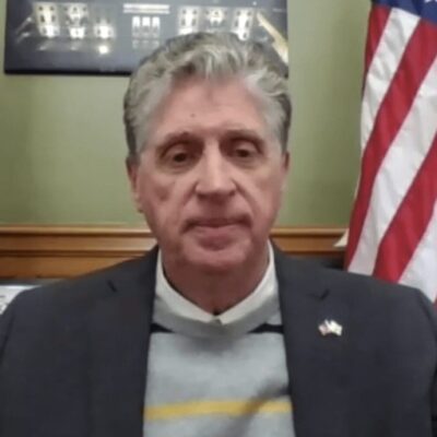 A man in a suit sitting in front of an american flag.