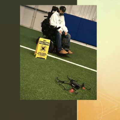 A man in a wheelchair is sitting on a field with a drone.