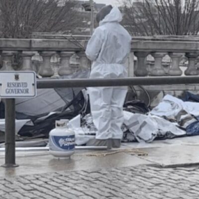 A homeless man in a white suit standing next to a pile of trash in RI.