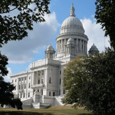 A large white building sits on a grassy hill.