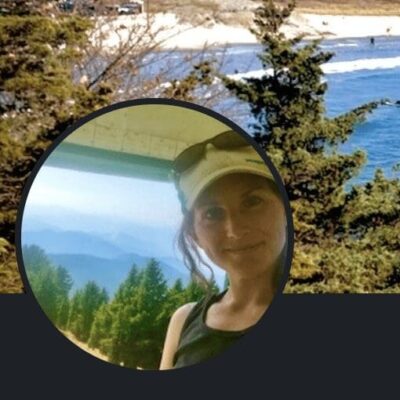 A homeless woman is standing in front of a tree with a view of the ocean.