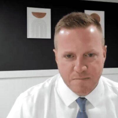 Joe Paolino, a man in a white shirt and tie, is sitting in an office.