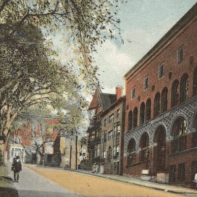 An old postcard shows a street with buildings and trees.