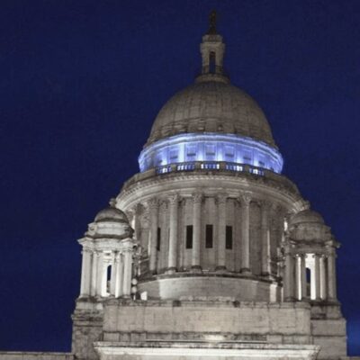 The state capitol building is lit up blue at night, symbolizing legislation.