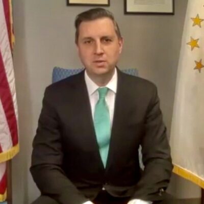 A man in a suit and tie sitting in front of an american flag.