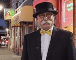 A homeless man in a tuxedo and bow tie standing on a city street.