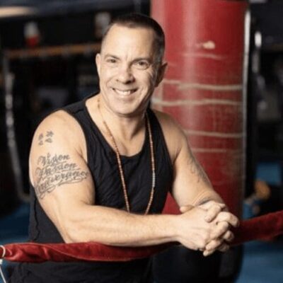 A smiling man with tattoos in a boxing ring.