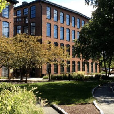 A brick building with trees and grass in front of it, providing a serene backdrop for those who work from home.