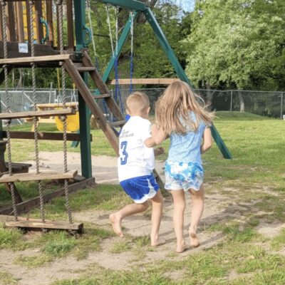 Two children running in front of a playground.