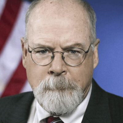 A man with glasses and a beard in front of an american flag.
