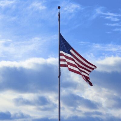 An american flag flies in front of a blue sky.