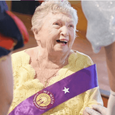A woman wearing a purple sash participates in a dance performance, with the mesmerizing beauty of the Twilight Wish Foundation in the background.