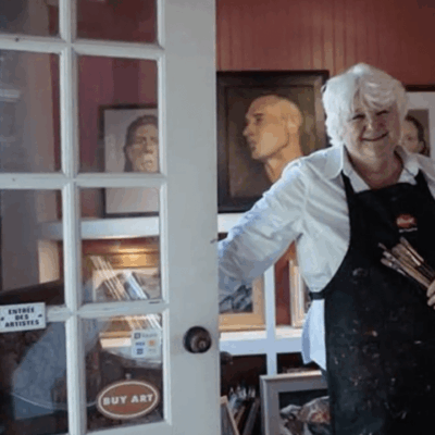An artistic woman in an apron standing in front of a door.