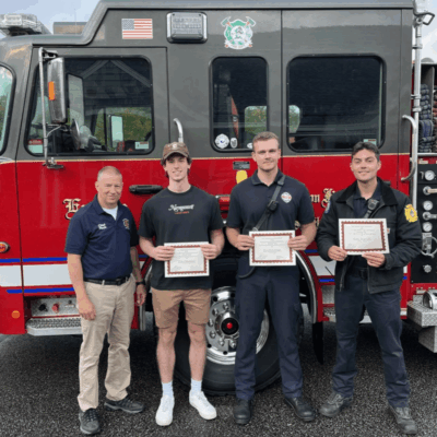 Four firefighters holding certificates in front of a fire truck.