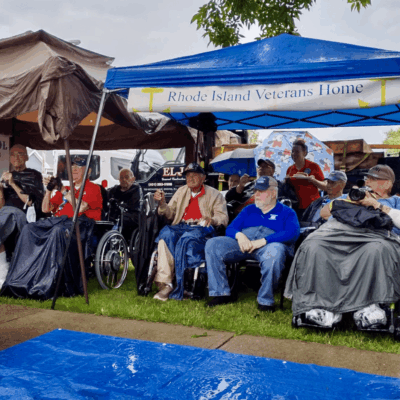 A group of veterans in wheelchairs in front of a blue tent.
