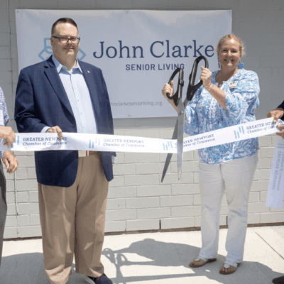 A group of people cutting a ribbon in front of a john clarke sign.