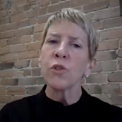 A woman with short hair in front of a brick wall.