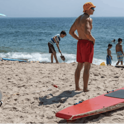 A man is standing on a beaches with a surfboard.