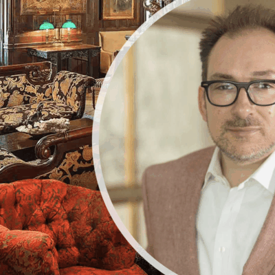 A man in glasses is standing in front of an ornate living room with remarkable architecture.