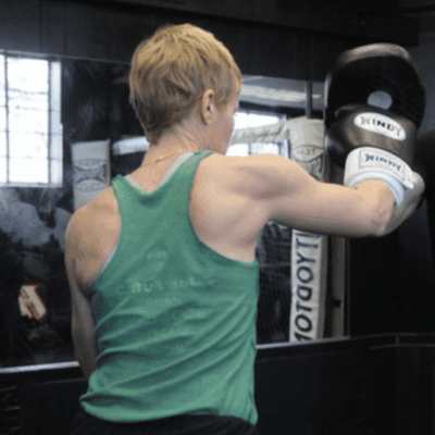 A man and a woman engaging in boxing training, focusing on women's self-defense techniques, at a gym.