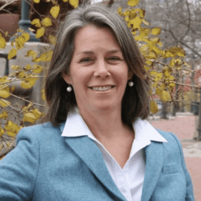 A woman in a blue jacket smiling in front of a tree.