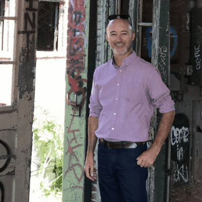 A man named Joe Paolino Jr. standing in front of an old building with graffiti on it.