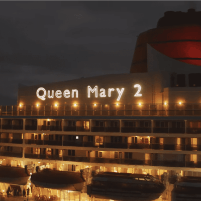 The queen mary 2 is lit up at night.
