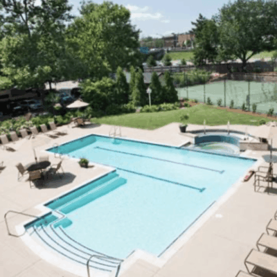 A swimming pool and a tennis court with lounge chairs available for relaxation.